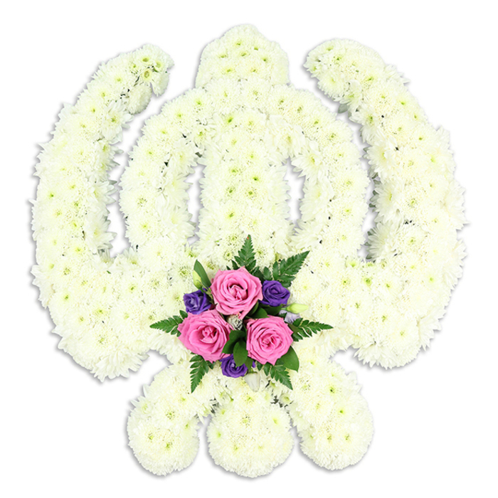 A striking floral depiction of the Sikh Khanda symbol fills the frame, beautifully rendered in pure white blossoms and set against an uncluttered white background that enhances its calm, spiritual character. The central double-edged sword rises vertically, crisp and well-defined, enclosed by the smooth circular chakkar, while two elegant kirpans curve outwards from the base, all formed from tightly clustered white chrysanthemums. Each bloom is positioned thoughtfully, with overlapping petals creating a lush, almost cushion-like surface, the shades of ivory and soft cream blending together in a gentle haze. The regularity of the flowers gives the emblem a sculptural appearance, as if it were a carved relief made from petals. At the joining point of the kirpans, a smaller, colourful spray adds a compassionate accent. Three soft pink roses, just past bud stage and opening towards full bloom, sit together at the heart of this cluster, their layered petals glowing against the white. Interspersed among them are petite deep purple blossoms - likely lisianthus or freesia - adding a rich, contemplative tone that feels appropriate for remembrance. Sprigs of fresh green fern and foliage provide contrast and natural movement, like a breeze across the open spaces near Basildon's Langdon Hills. The lighting is bright but gentle, producing only a light shadow beneath the tribute so it appears grounded yet serene. This bespoke floral Khanda, suited to Sikh funerals, memorial services, and moments of quiet reflection in the Basildon community, conveys profound respect, faith, and enduring love, thoughtfully crafted to honour a cherished life.