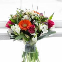 Artistry and balance define this magnificent bouquet, where vivid hues and tactile variety speak to Basildon's flourishing community spirit. Creamy peach gerberas create a gentle, glowing perimeter, their petals enclosing bold, lively orange centers that sparkle with the vibrance of a local festival. Tucked amongst them are sumptuous fuchsia roses-velvety and full, adding a layer of romance and indulgence. White lilies and petite clusters of spray roses introduce soft, airy brightness, building a sense of garden-fresh abundance that echoes the flora of Wat Tyler Country Park. The arrangement's structure is grounded by broad, arching green aspidistra leaves, enveloping the bouquet's base like a protective embrace, while slender greenery and wisps of finer leaves animate the composition with subtle motion and freshness. Bathed in a soft wash of daylight-much like a Basildon living room filled with afternoon sun-the bouquet's rich palette comes to life, each hue crisp against the gentle, diffuse background. With an uplifting fragrance suggestive of roses and lilies mingled with verdant greens, this arrangement is ideal for gathering friends, brightening a home, or sending best wishes for new beginnings throughout Basildon. Each stem demonstrates the precision and passion emblematic of Flower Delivery Basildon, bringing artistry to every doorstep.