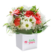 There's a vivacious charm to this floral arrangement-its blend of coral, peach, and vibrant red carnations paired with gleaming white daisies creates a sense of celebration reminiscent of springtime festivities in Basildon's parks. The carnations' lavish, ruffled petals spill with warmth, while the daisies' bright lime-green eyes bring an undeniable cheer, like catching sunlight glinting off the lake in Gloucester Park. Airy clouds of baby's breath weave gently among the bolder blooms, giving the bouquet a soft, romantic touch. Accents of tightly furled, purple-tipped buds on the left side suggest promise and anticipation, recalling the quiet beauty of dawn over Langdon Nature Reserve. The entire display is wrapped in lush, deep green foliage, the glossy leaves lending a polished, natural finish. Presented in a crisp white square gift bag with sturdy ribbon handles, the arrangement radiates fresh elegance and sincere joy. Each stem has been hand-placed with intention, resulting in a full, rounded composition-the kind of bouquet perfect for brightening birthdays, celebrating new beginnings, or simply sharing a little joy across Basildon. Every detail, from careful flower selection to expert arrangement, reflects the artistry and pride of Basildon's own flower specialists, who ensure freshness and beauty in every hand-delivered gift.