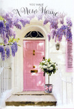 The scene shows a Basildon doorstep transformed into a floral symbol of fresh beginnings. A pale pink door, painted in a smooth, matte finish, stands as the focal point, its colour radiating a soft, understated warmth. The surrounding wall is whitewashed, providing a clean backdrop that allows the flowers to stand out clearly. Spilling from above, wisteria cascades in abundant strands of lavender and lilac, the blooms forming a delicate canopy that frames both the door and a coordinating shutter. Some blossoms hang low, almost within reach, casting dappled shadows that bring to mind the play of light in gardens dotted around Noak Bridge and Kingswood. Sitting at the threshold is a chic grey metal bucket, used as a rustic-style vase, overflowing with lush white and cream roses. The roses are fully opened, their petals layered and soft, suggesting both luxury and tenderness. Fresh green foliage peeks between the blooms, adding a natural, leafy contrast to the creamy tones. A soft pink ribbon wraps the bucket and is tied into a gently drooping bow, its silky texture an elegant finishing touch that mirrors the shade of the front door. The lighting is gentle and natural, creating a restful atmosphere that feels hopeful and inviting. It is easy to imagine these flowers being delivered to celebrate a new home in Basildon-perhaps near Gloucester Park or Laindon-offering a wordless message of welcome, congratulations, and the promise of happy days just beyond that pink-painted doorway.